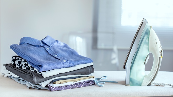 stack of ironed clothes and an iron on an ironing board